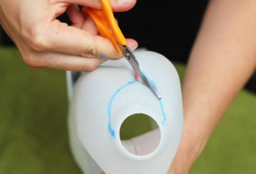 A close up of a milk carton and some hands using scissors to cut around the top opening of the carton